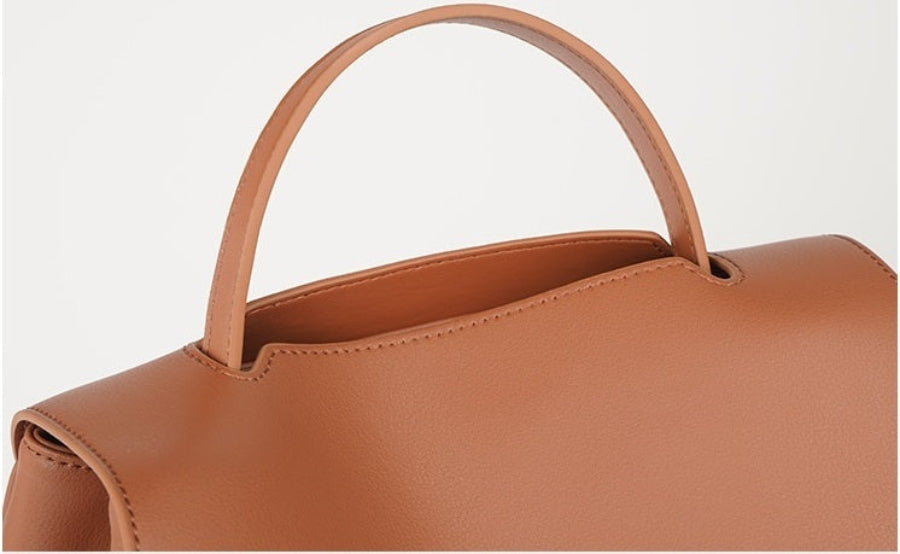 Brown leather handbag with a handle on a light gray background