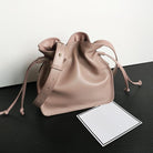 Pink leather drawstring bag on a black surface with a white card.