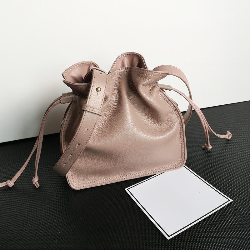 Pink leather drawstring bag on a black surface with a white card.