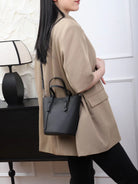 Person wearing a beige coat holding a black handbag in a minimalistic setting.