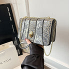 Silver glittery handbag with gold chain held by a hand against a neutral background