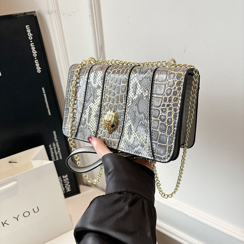 Silver glittery handbag with gold chain held by a hand against a neutral background