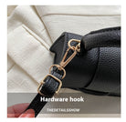 Close-up of a black handbag with a gold hardware hook on a neutral background