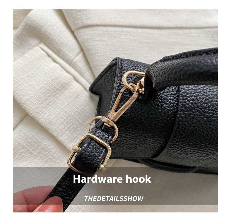 Close-up of a black handbag with a gold hardware hook on a neutral background