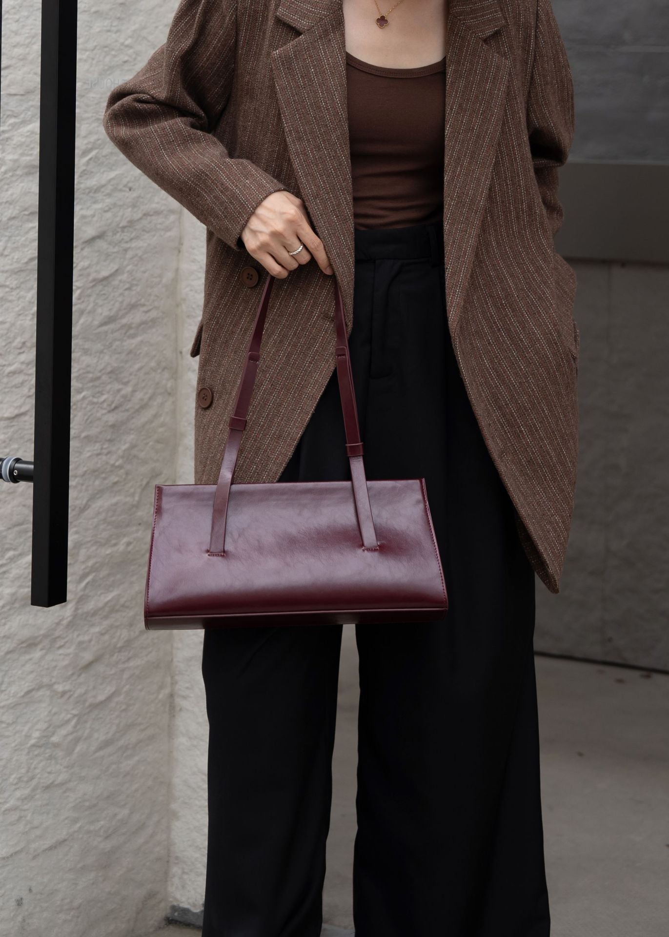 Person holding a maroon handbag against a neutral background