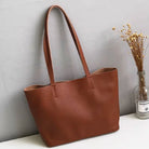 Brown leather tote bag on a white surface with a gray wall and plant in the background