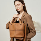 Woman holding a brown leather handbag against a neutral background