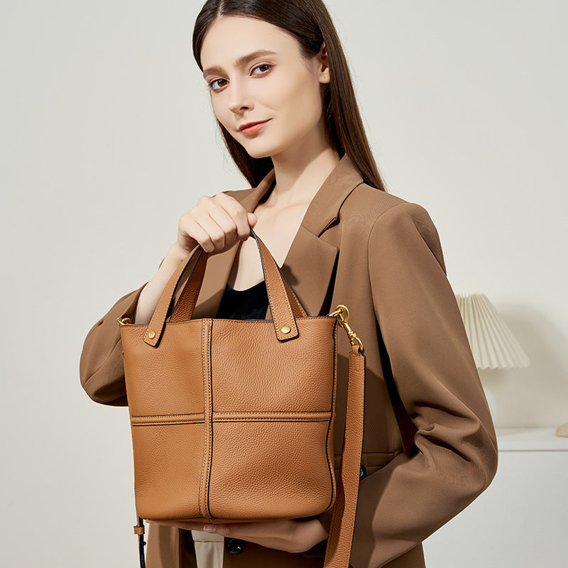 Woman holding a brown leather handbag against a neutral background