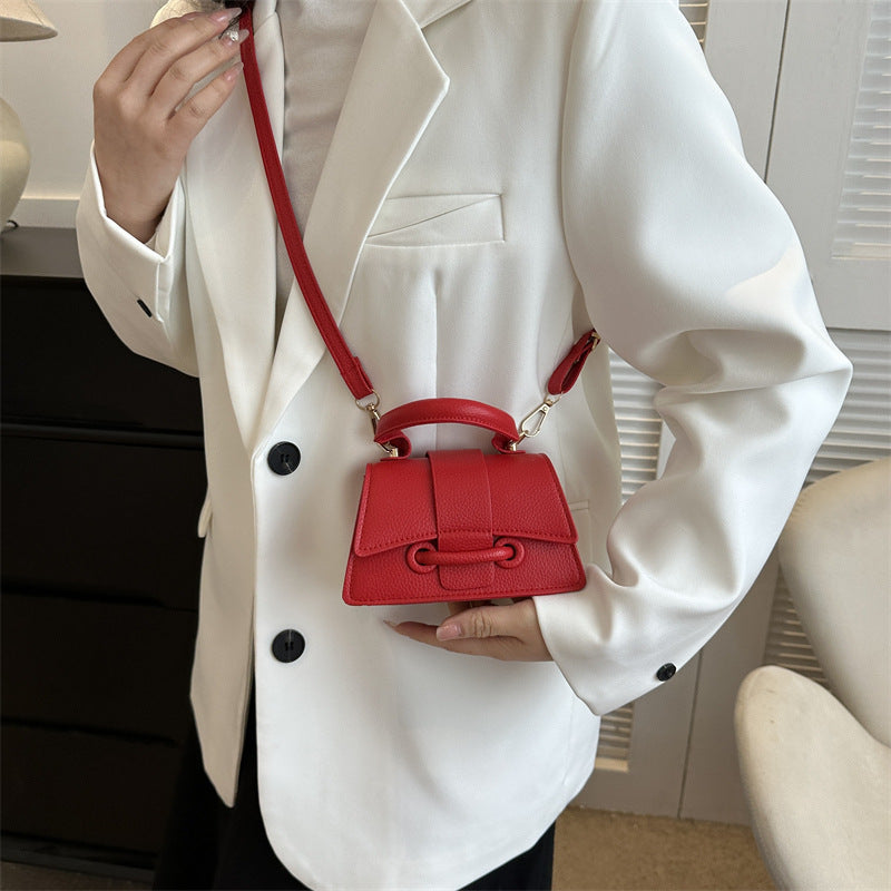 Person holding a red handbag wearing a white blazer indoors.