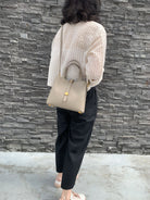 Person holding a beige handbag against a gray stone wall