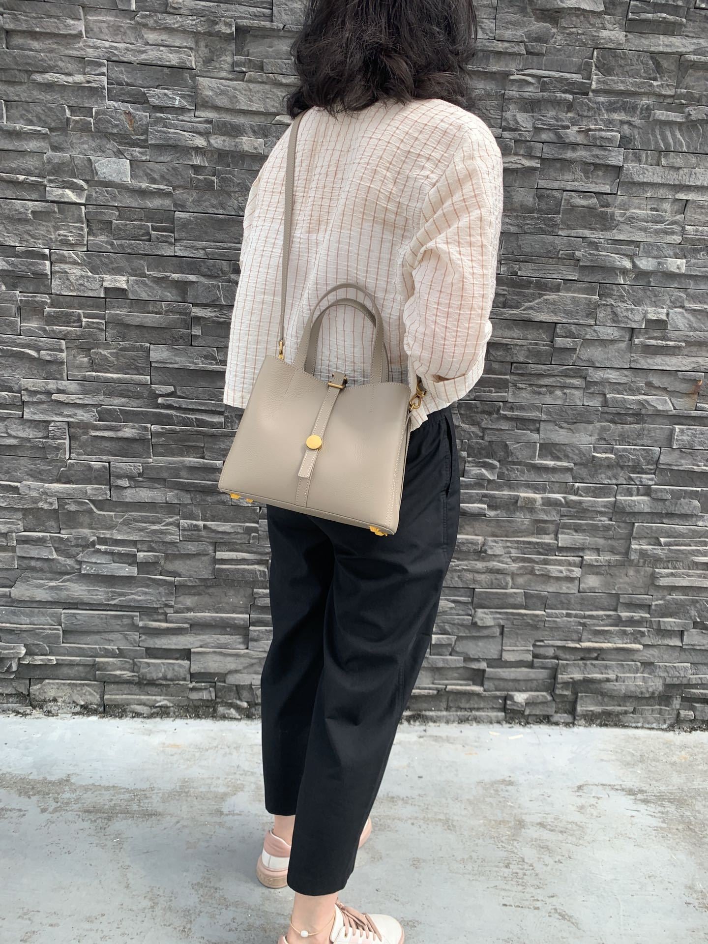 Person holding a beige handbag against a gray stone wall
