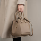 Person holding a beige handbag with a neutral background