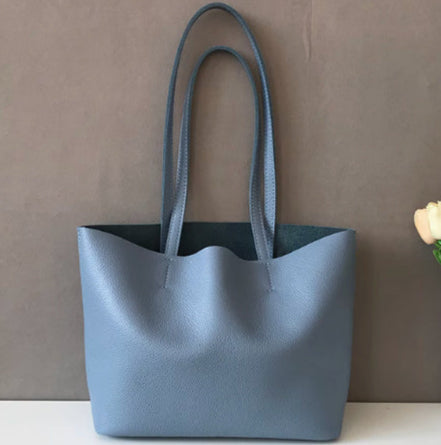 Blue tote bag on a white surface with a vase of flowers in the background