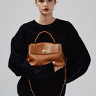 Person holding a brown leather handbag against a plain background