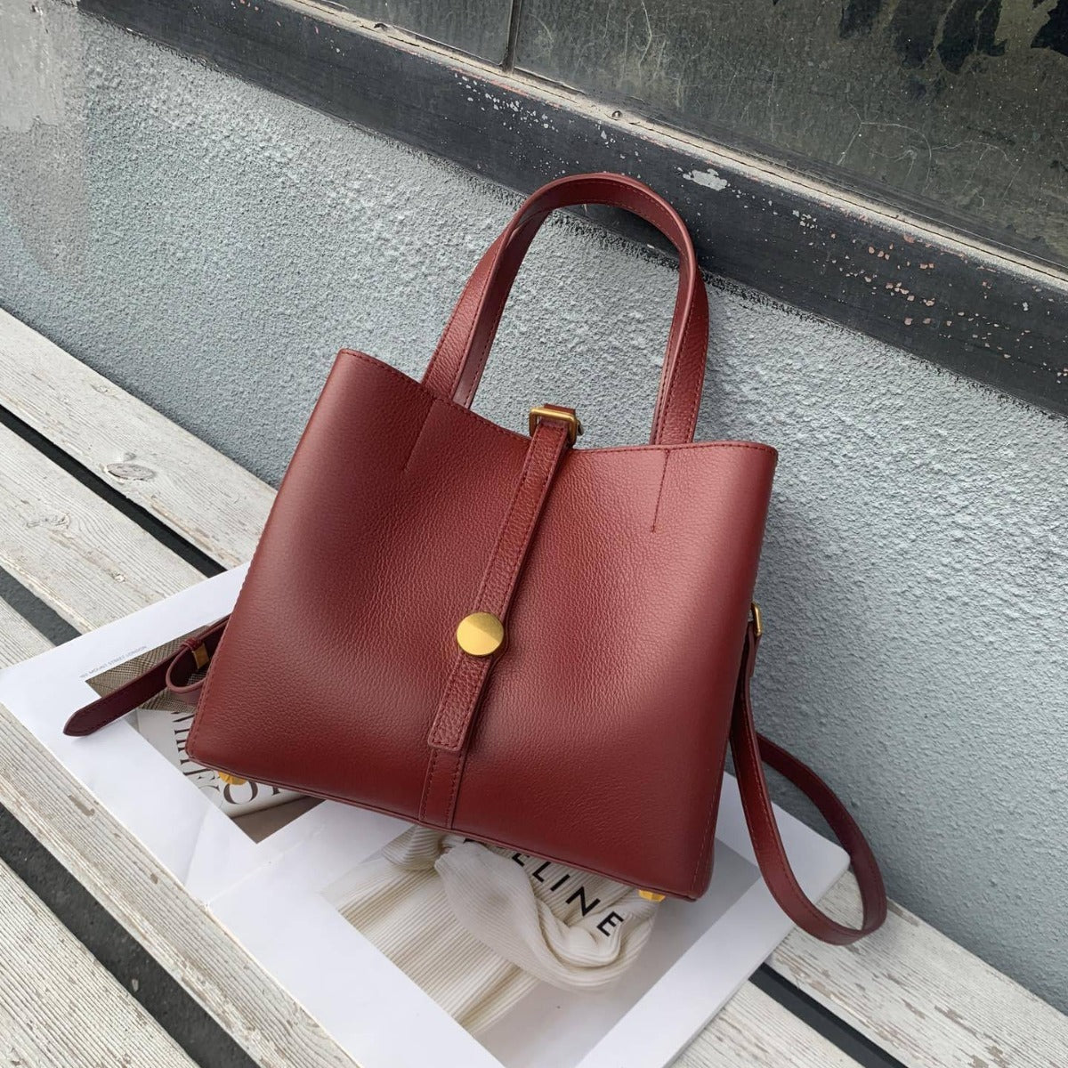 Red handbag with a gold clasp on a wooden surface against a gray wall.