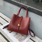 Red handbag with a gold clasp on a wooden surface against a gray wall.