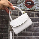 White handbag held by a hand against a brick wall background