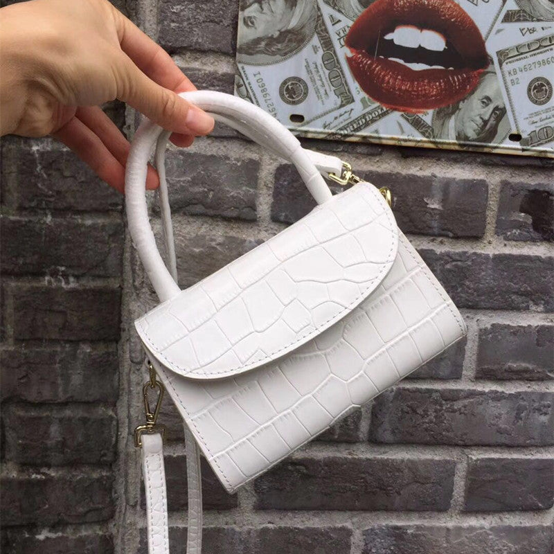 White handbag held by a hand against a brick wall background