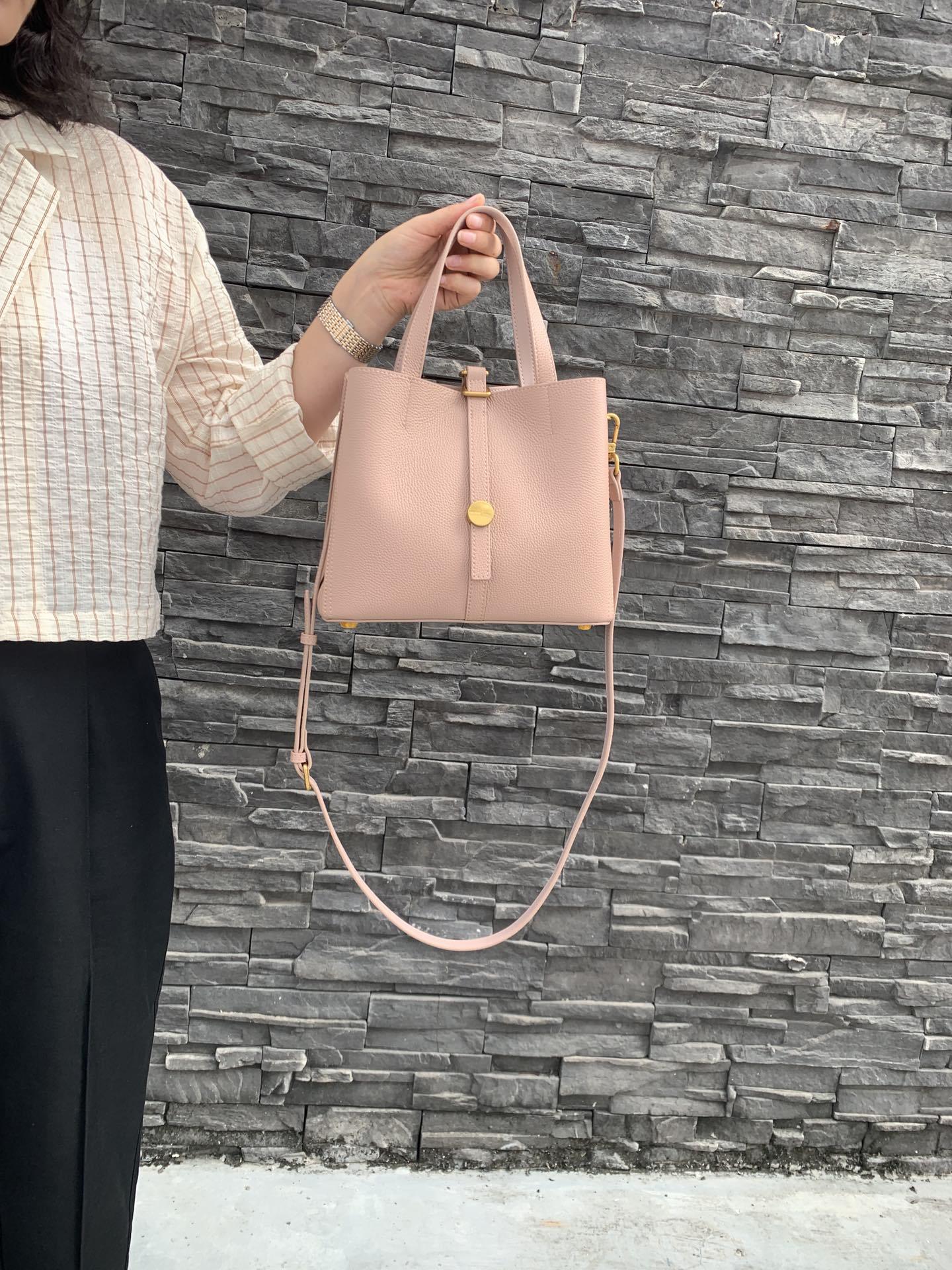 Person holding a pink handbag against a stone wall