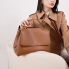 Woman holding a brown handbag against a neutral background