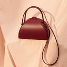 Maroon handbag with a strap on a light pink background