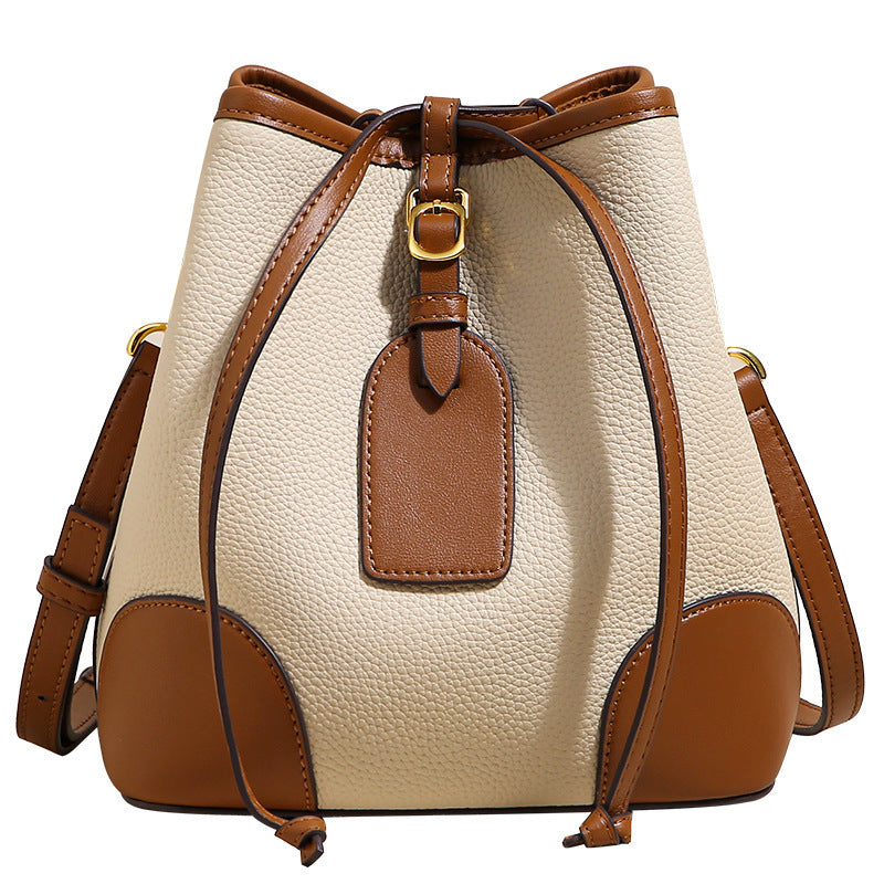 Beige and brown leather bucket bag with a tag on a white background
