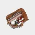 Open brown leather bag with various items on a light gray background
