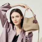 Woman holding a beige handbag with a decorative charm against a light background