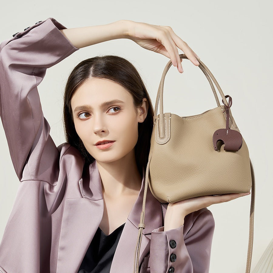 Woman holding a beige handbag with a decorative charm against a light background