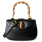 Black handbag with bamboo handle and strap on a white background
