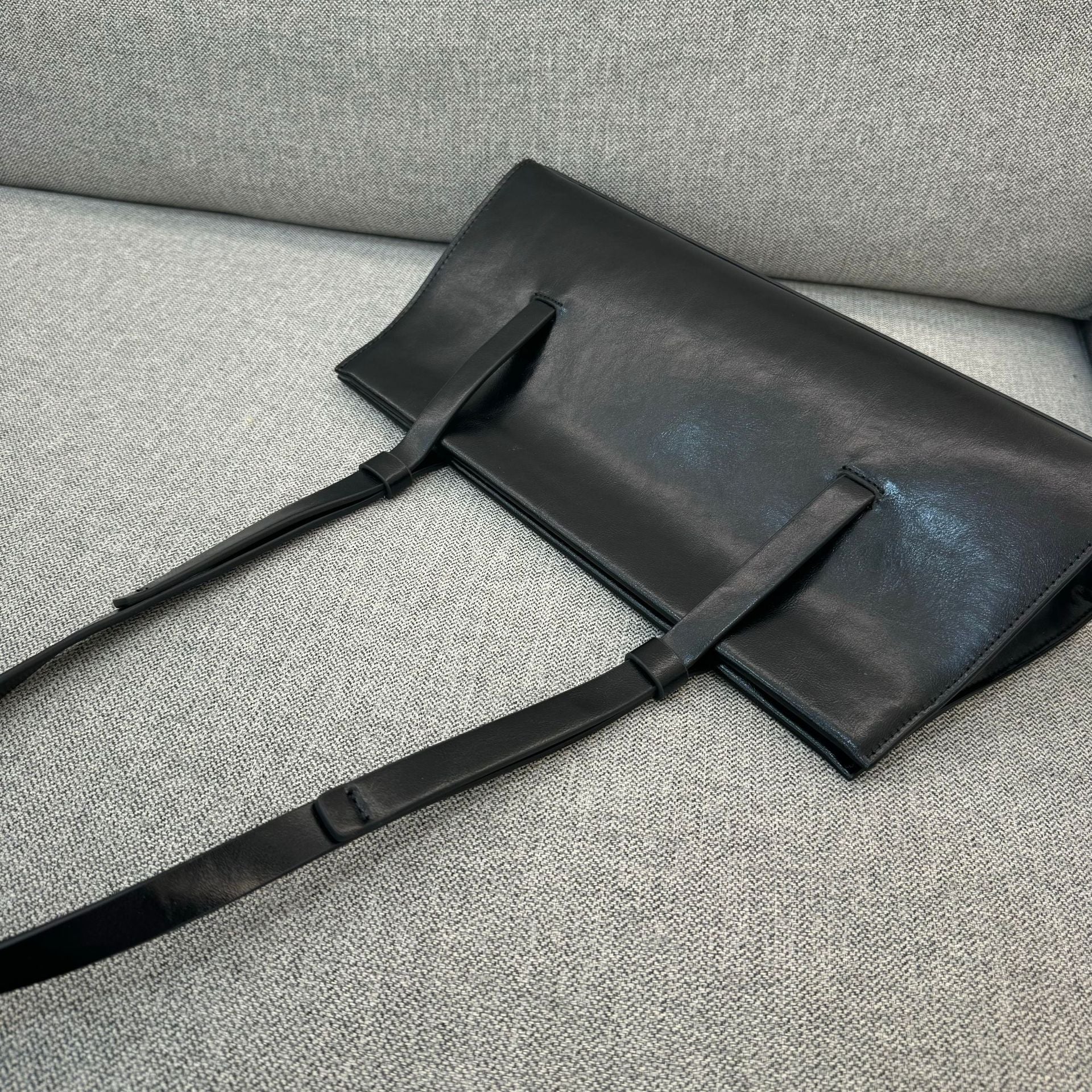 Black leather bag with a strap on a gray textured surface