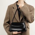 Person wearing a brown coat holding a black handbag against a neutral background