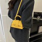 Person wearing a dark gray coat with a yellow handbag over their shoulder indoors.