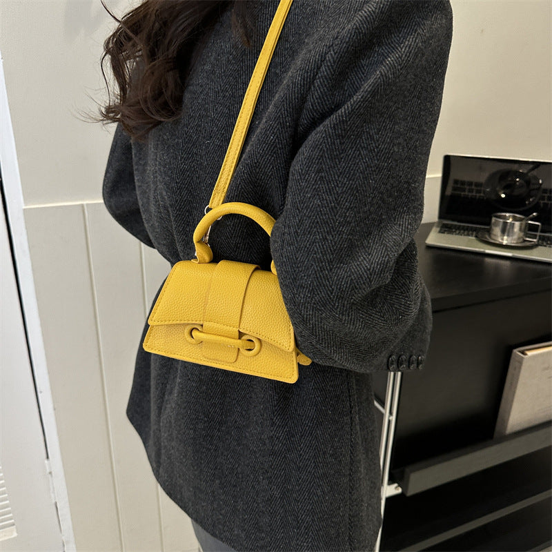 Person wearing a dark gray coat with a yellow handbag over their shoulder indoors.