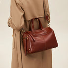 Brown leather handbag held by a person wearing a beige coat on a neutral background