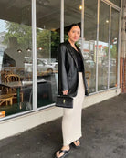 Woman in black blazer and white pants standing outside a cafe.