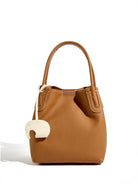 Brown leather handbag with a decorative charm on a white background