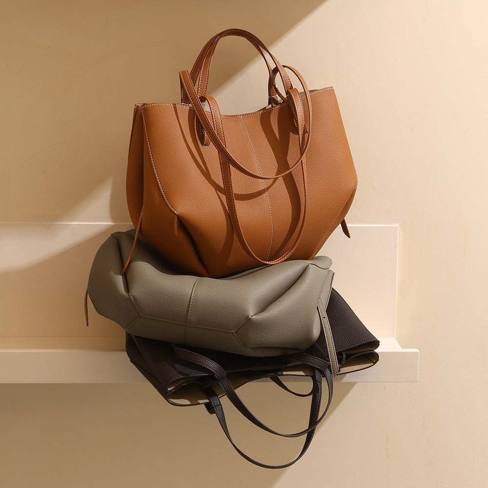 Brown leather handbag on top of a gray backpack against a beige wall.