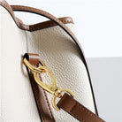 Close-up of a white handbag with brown leather strap and gold clasp on a light gray background