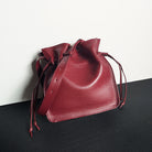 Red leather drawstring bag on a black surface with a white background