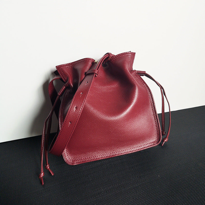 Red leather drawstring bag on a black surface with a white background