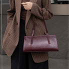 Person wearing a brown coat holding a maroon handbag against a neutral background