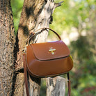 Brown handbag with a gold clasp attached to a tree in a natural setting