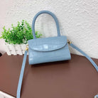 Blue handbag with a strap on a brown surface with a white textured wall and green plant in the background