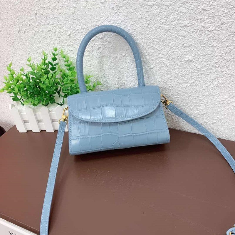 Blue handbag with a strap on a brown surface with a white textured wall and green plant in the background