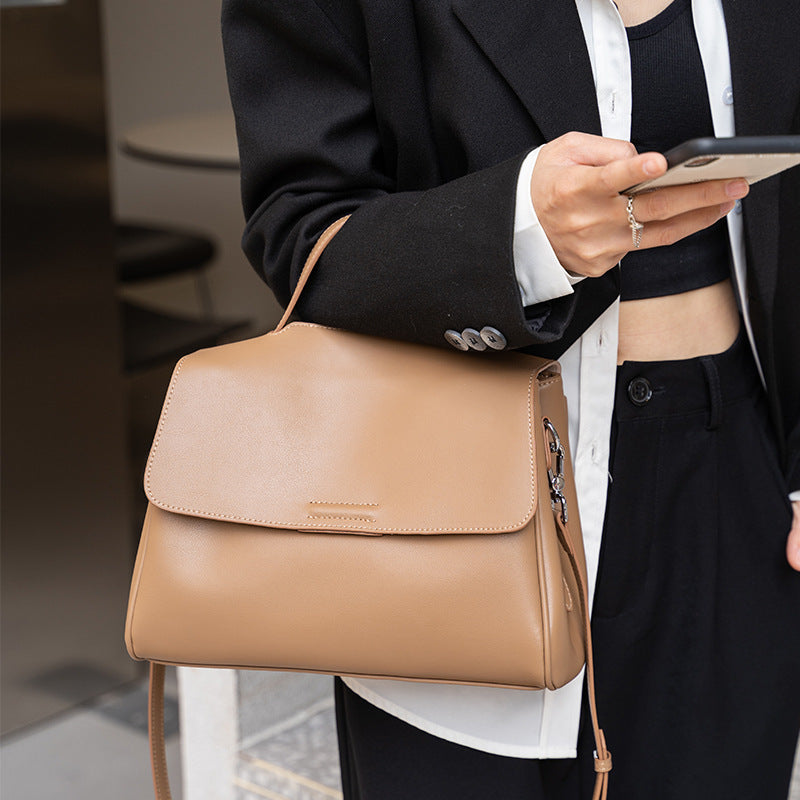Person holding a tan handbag and using a phone, blurred background