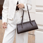 Person holding a brown leather handbag with a blurred background