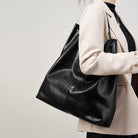 Person holding a black leather handbag against a plain background