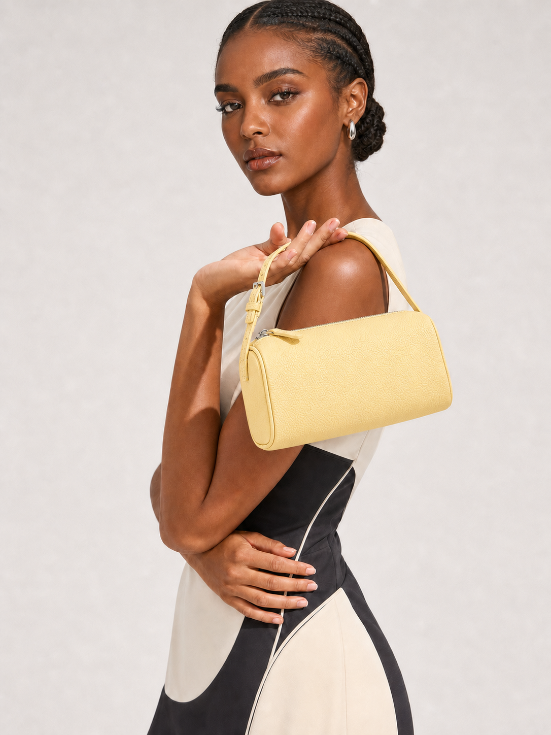 A model wearing a color-blocked dress and holding a light yellow textured shoulder bag against a light gray studio background.