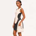 A woman modeling a sleeveless color-block mini dress with cream and black panels, paired with a matching cream handbag, against a plain white studio background.